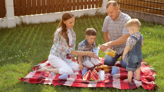 快乐的家庭坐在毯子上爸倒橙汁妈在温暖的阳光明日拿图片