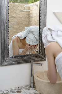 年轻成年女子在浴室洗脸时背着水泼到浴室水槽上图片
