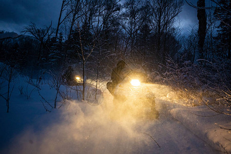 晚上的雪地摩托穿过冬季森林大灯穿过冬季森林的夜路雪背景图片