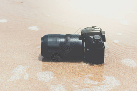 带长焦镜头的单反相机在海滩上旅行时被水海浪弄湿图片