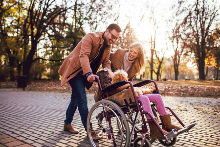 坐在轮椅上的美丽残疾女孩在秋天公园与母亲父亲图片