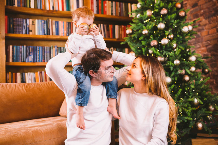家庭圣诞节概念可爱的家庭在冬天的晚上坐在圣诞树附近有儿子的幸福家庭在沙发附近的地板上在家庭在新年时间在家庭图片