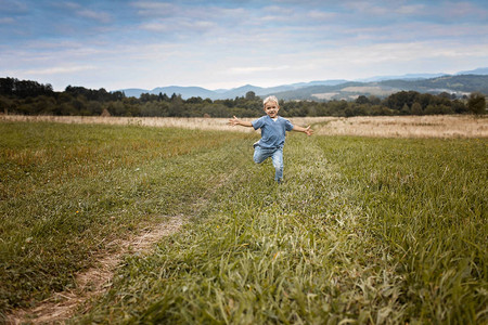可爱的小男孩跑过山间美丽的草地图片
