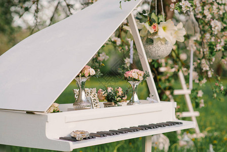 在设计婚礼时装饰的白色大钢琴或春天在盛开的苹果树花园里浪漫晚宴的图片