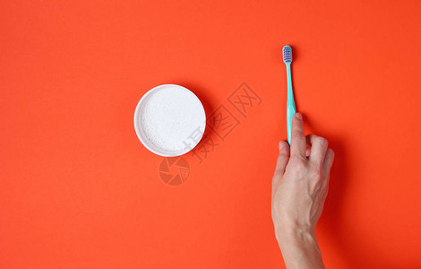 在橙色背景上女手握牙刷和牙粉的牙图片