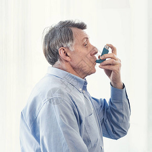 在现代诊所使用吸入器过敏的成熟人的侧边视角图片