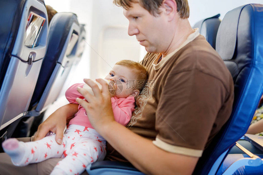 父亲在飞机上度假时抱着小女儿女婴从瓶子里喝配方奶带婴儿童和家庭概念的航空旅行带着孩子旅行图片
