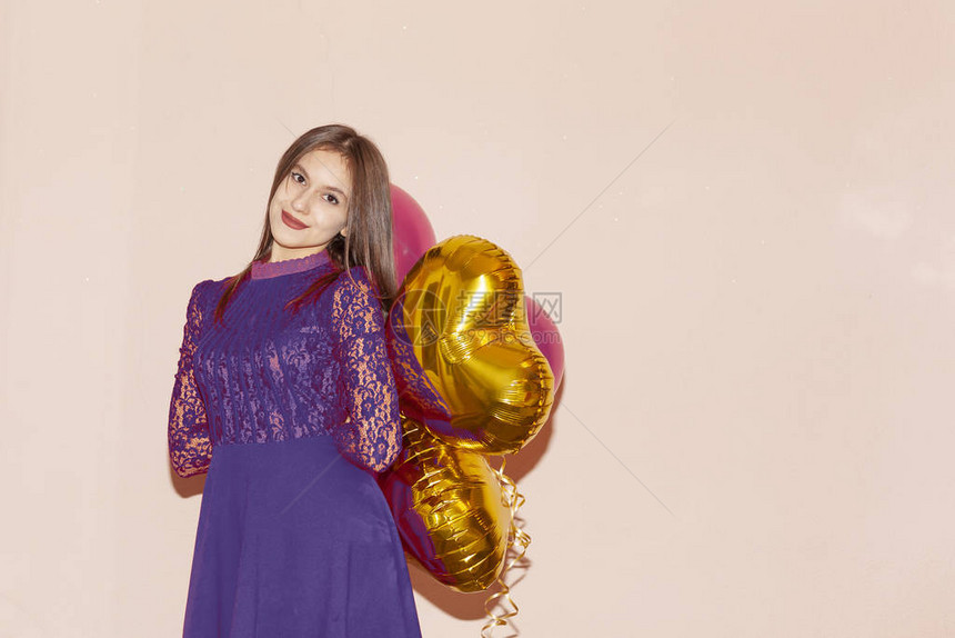 穿着紫罗兰色连衣裙的漂亮女人拿着两个心形的气球情人节生日妇女节周年纪念日图片