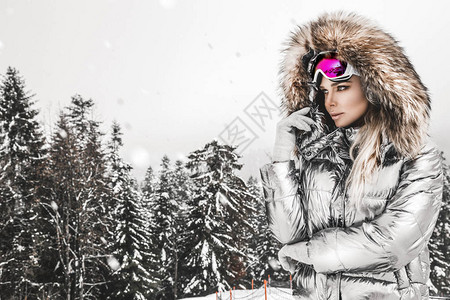 年轻女子冬季肖像冬季时装模特与滑雪服和护目镜冬天室外的可爱的少妇山背景图片