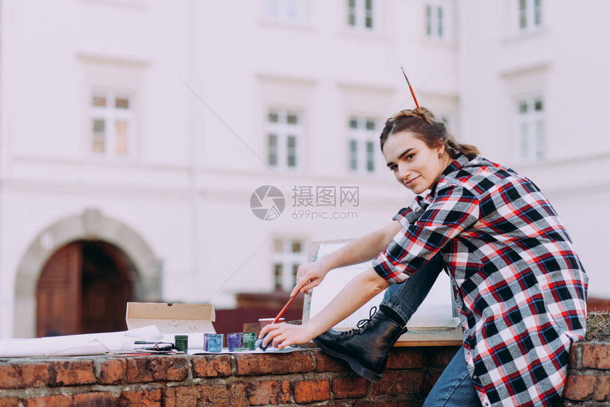 女艺术家坐在旧建筑背景的砖墙上画一幅画女孩花闲暇时间在城图片