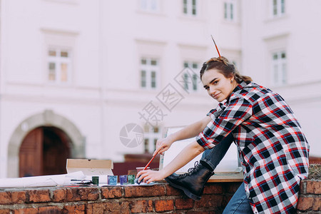 女艺术家坐在旧建筑背景的砖墙上画一幅画女孩花闲暇时间在城图片