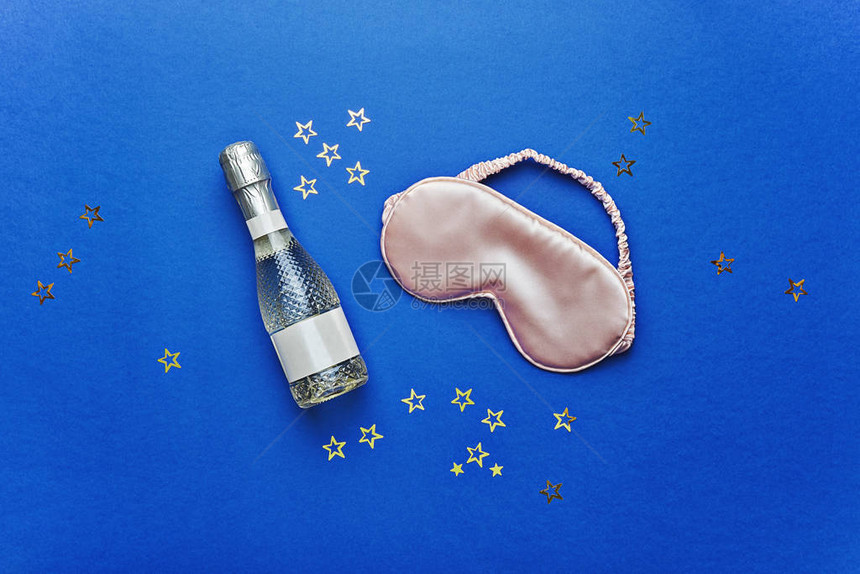 一瓶香槟酒和睡在蓝底帕贾马概念的面具图片