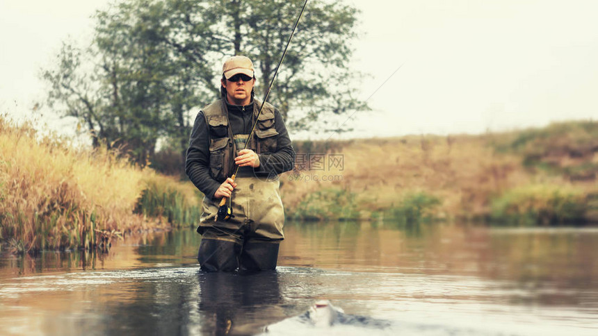 钓飞鱼渔夫在河的背景上拿着一根鱼竿图片