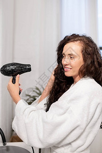 漂亮的年轻微笑的女士与头发干洗机照顾她的黑长卷毛在图片
