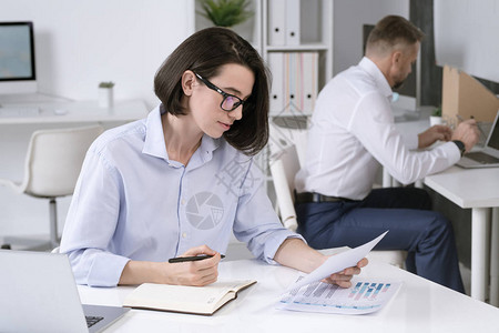 忙碌的女办公室经理在与背景同事一起坐在办公桌前时图片