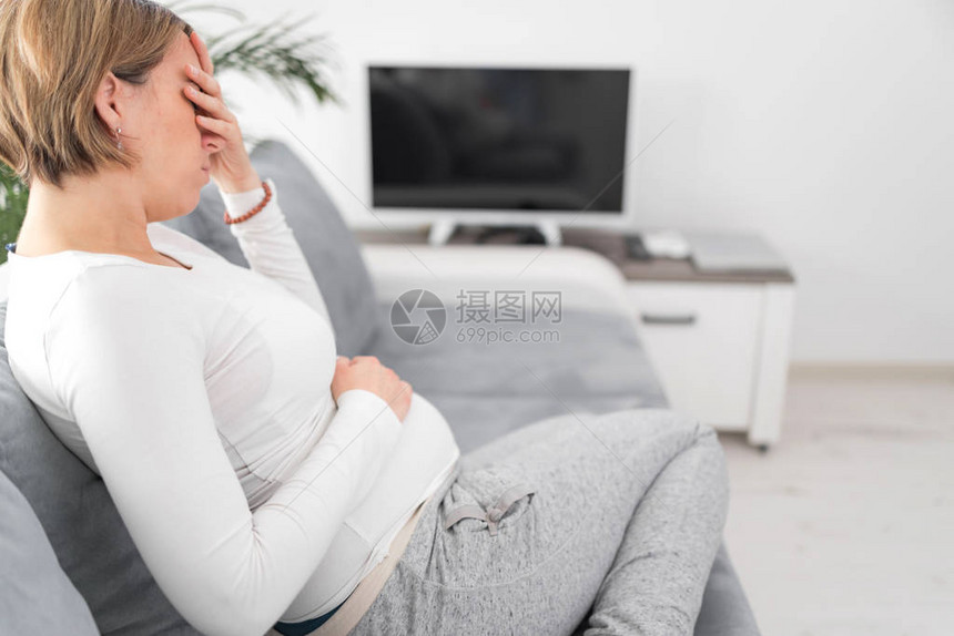 怀孕疲劳的孕妇在沙发上肚子和头部有图片