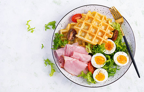 早餐包括玉米面华夫饼煮鸡蛋火腿和白色背景的番茄图片