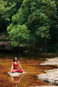 美丽的年轻黑女人坐在小溪的岩石上在森林的中心图片