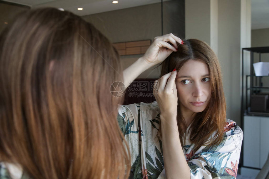 一位漂亮年轻女子在镜子前检查头皮和头发根颜色白发脱发或头皮干图片