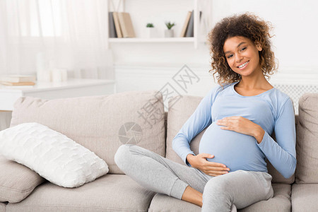 幸福的孕妇坐在沙发上抚摸她的肚子图片