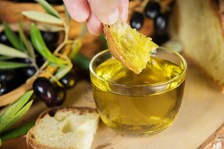 一只手将一块面包浸入盛满特级初榨橄榄油的碗中图片