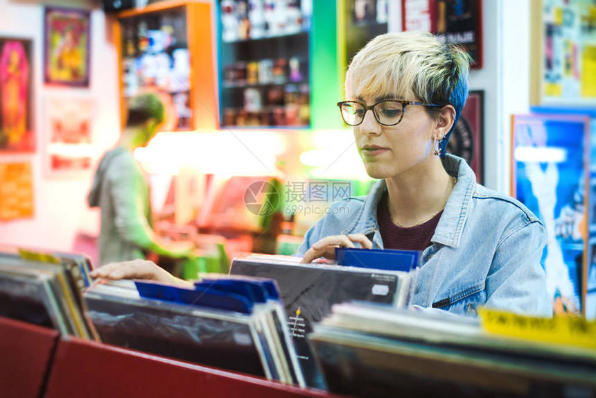 年轻女和男浏览通过文体磁盘和在唱片店中选用乙烯LP图片