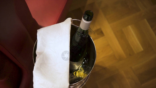 在棕色地板背景上用白毛巾在冰桶中打开香槟瓶的特写图片
