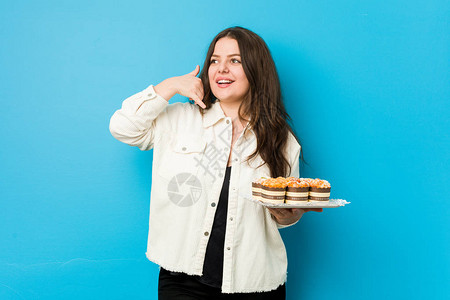 年轻卷发女人拿着纸杯蛋糕手握着一个手机势图片