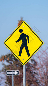 垂直框架交通黄色警告标志在一根横杆上一个行人跨过蓝色背景图片