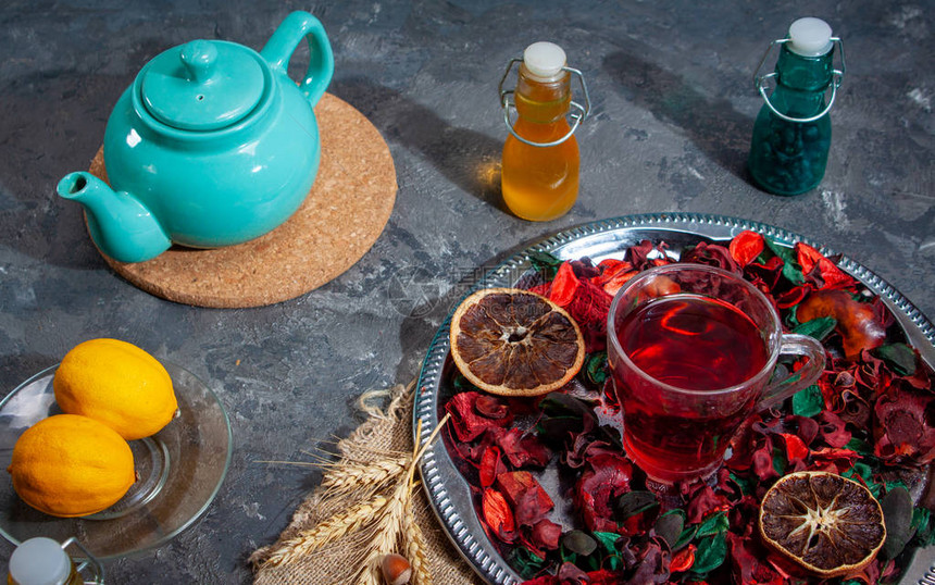 在玫瑰花瓣和干茶果酱之间在一个木制桌上的玻璃杯子里喝红图片