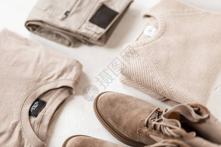 麂皮男士时尚靴子搭配时尚米色休闲毛衣和白色地板上的经典裤子背景图片
