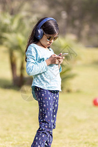 小女孩在公园里用耳机在智能手机上收图片