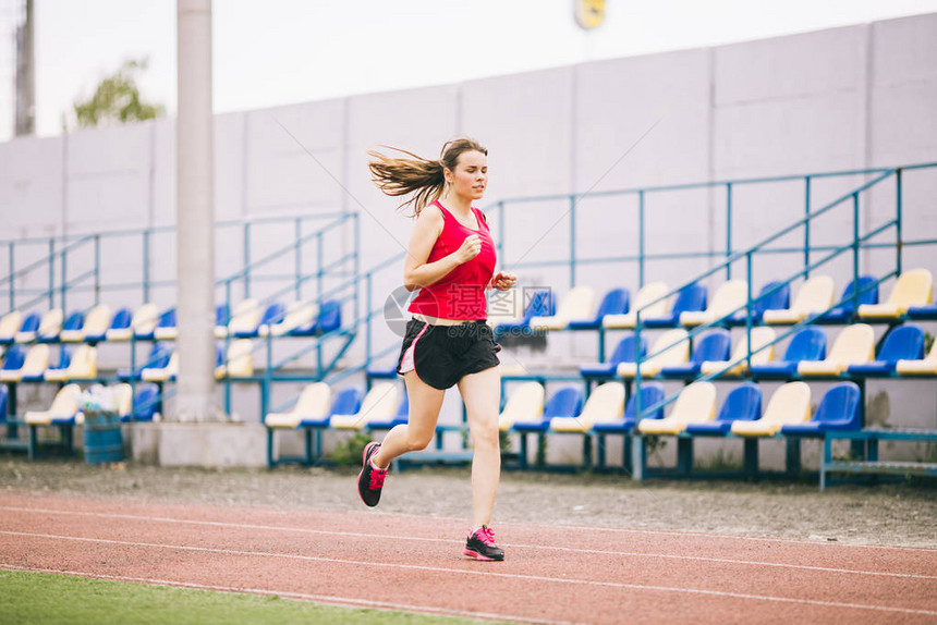 跑在体育场的妇女在体育场跑道上跑步的年轻女子目标成就概念在球场上进行健身慢跑锻炼健康主题成功的图片