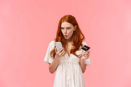沮丧和疯狂愤怒困惑的红发女人不高兴地盯着智能手机显示屏图片