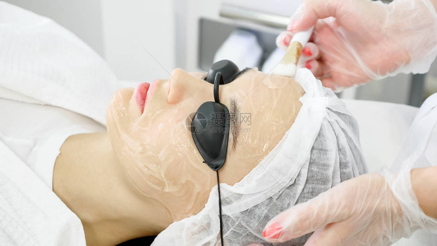 专业治疗师对美容院女客户在激光反射侧视前的面部图片