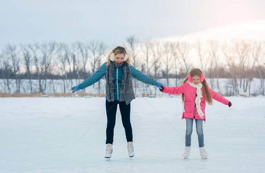 微笑的年轻母亲和她可爱的女儿一起用手滑冰家庭滑冰和训练在冬日在冰区的白色溜冰鞋周末在寒冷天气图片