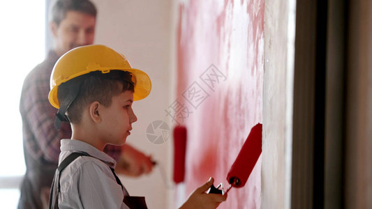 一个小男孩和他微笑的父亲用红色粉刷墙壁一个戴着头盔图片