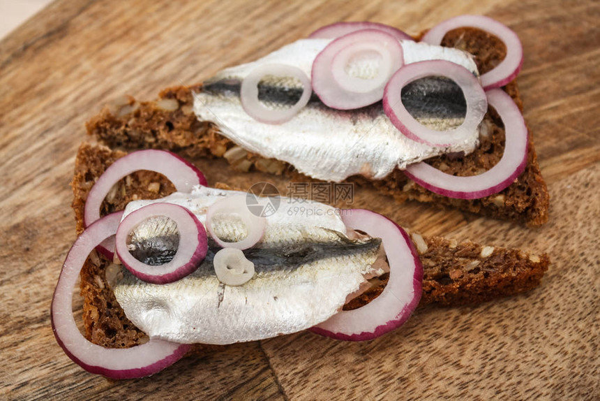 一条黑面包上的斑点鱼与面包和红洋葱在切口桌上图片