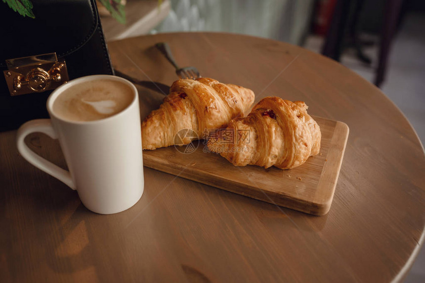 卡布奇诺咖啡与美丽的拿铁艺术和羊角面包在桌子上的木制背景早上的完美早图片