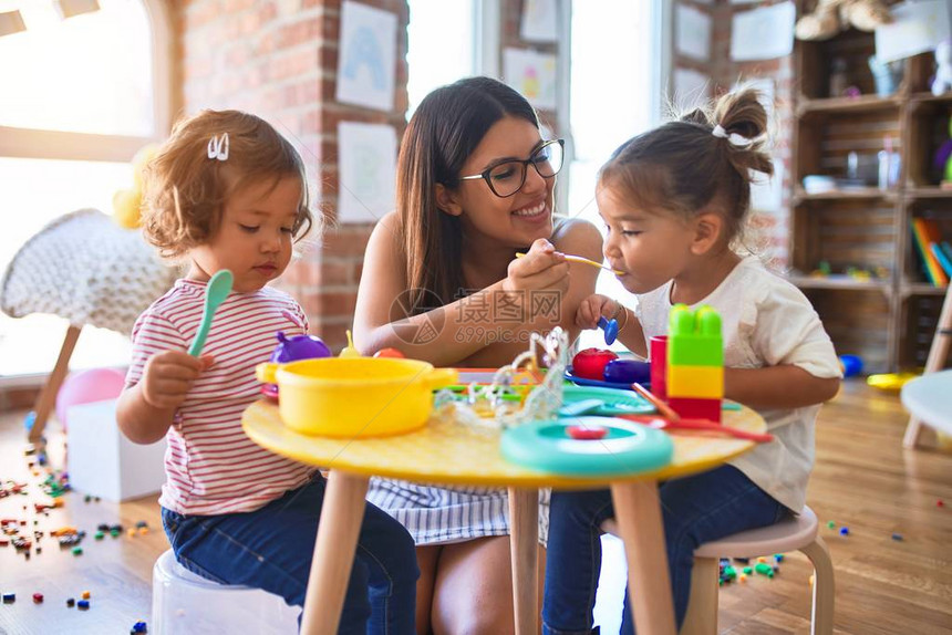 年轻漂亮的老师和幼儿在幼儿园用塑料食品和图片