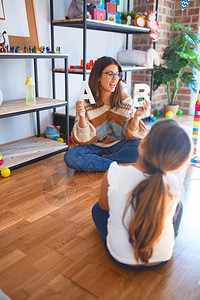 美丽的老师在幼儿园的很多玩具旁教幼儿字母表图片