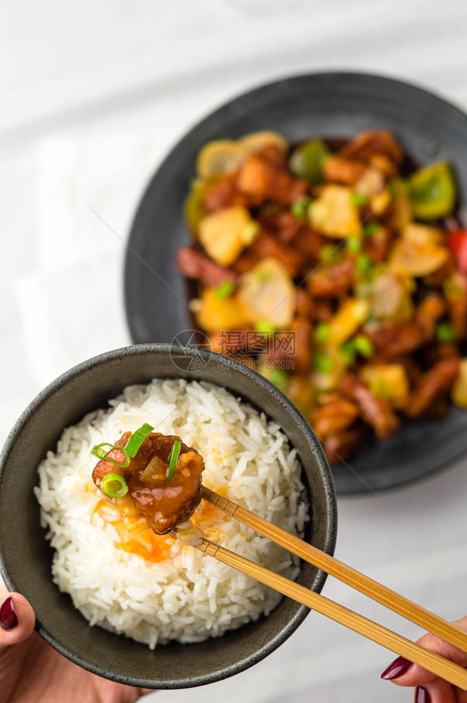 筷子上的糖醋猪肉在炒菠萝洋葱辣椒和酱汁中加入油炸肉酸甜菜在亚洲美食中很常见图片