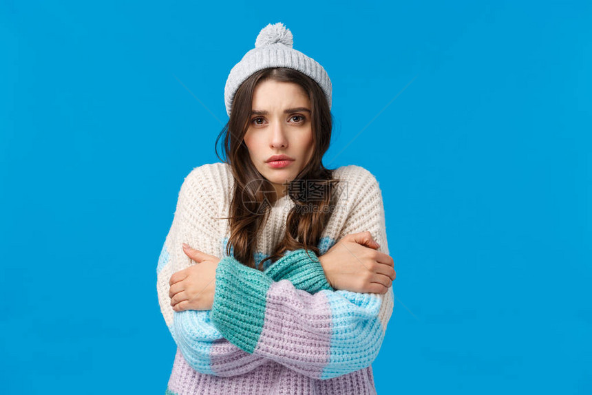 穿着冬帽毛衣从低温中颤抖拥抱自己温暖憎恨寒冷季节蓝背景的忧郁和阴沉的傻姑娘图片