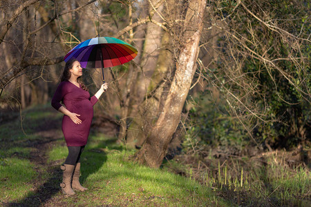 孕妇在公园内露户带林地树木散步的有色雨伞或遮阳灯光图片