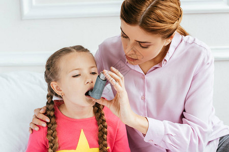 悲伤的女儿患有哮喘使用吸入器和担图片