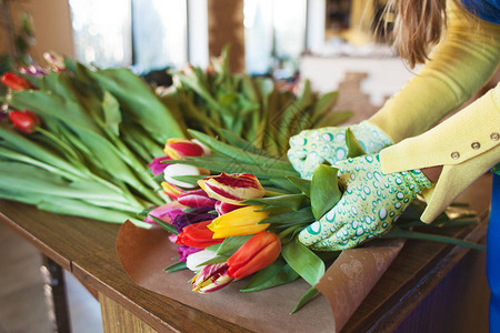女孩花店正在用牛皮纸在花店里包装美丽的郁金香妇图片