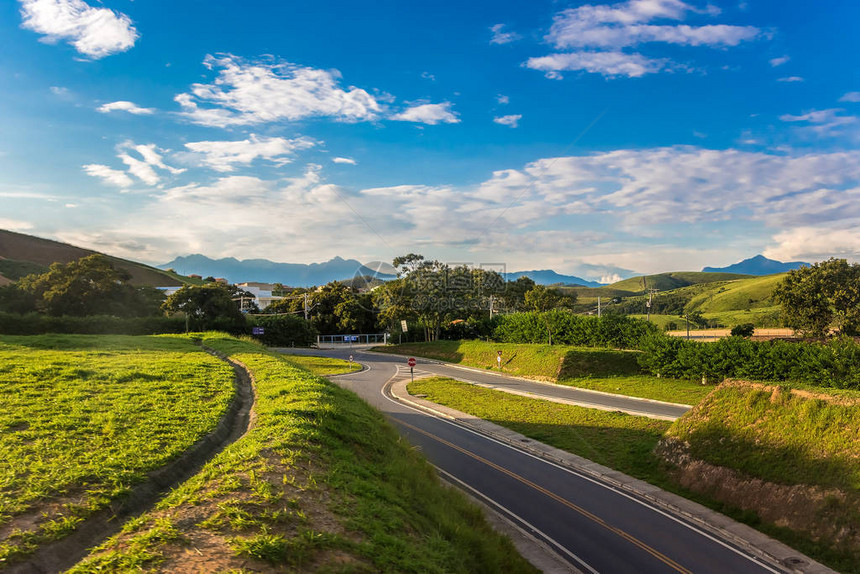 在大田间的农村路令人惊叹的蓝天与美丽的云彩山脉草甸与新鲜的绿草在里约热内卢区的高速公图片