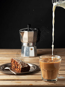 牛奶倒入一杯咖啡板配胡萝卜蛋糕咖啡位于棕色木制背景上特写镜头图片