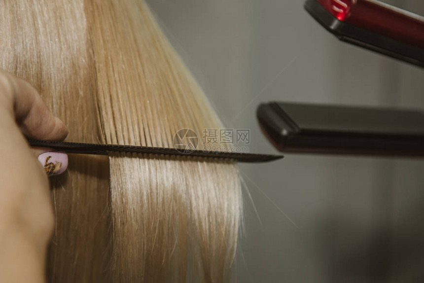 发型有吸引力的金发短用电熨斗做发型直发器灰色背景特图片