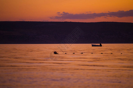 在橙色日落背景的渔船上图片